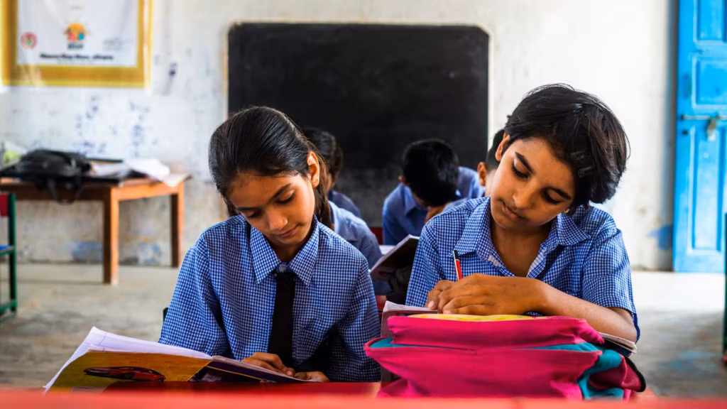 Two girls writing in their notebooks at a school desk
