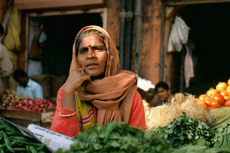 A woman selling fresh green leafy vegetables and tomatoes at a market stall
