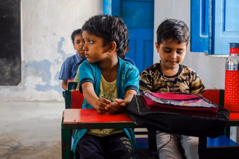 Two young boys sitting at a desk in a village school classroom with blue doors