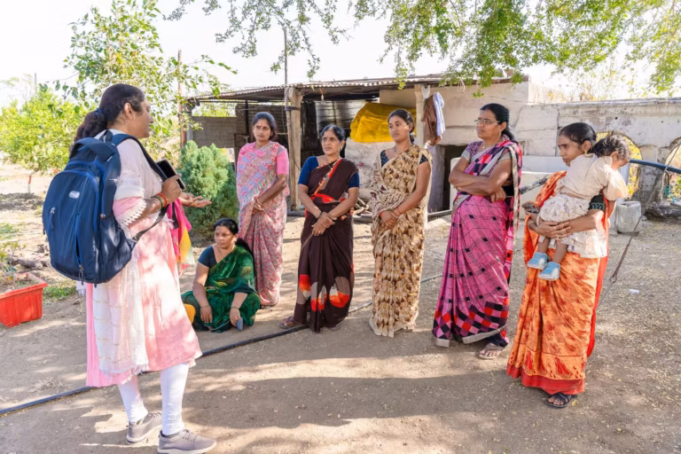 A young woman with a backpack talking with a group of village women outdoors